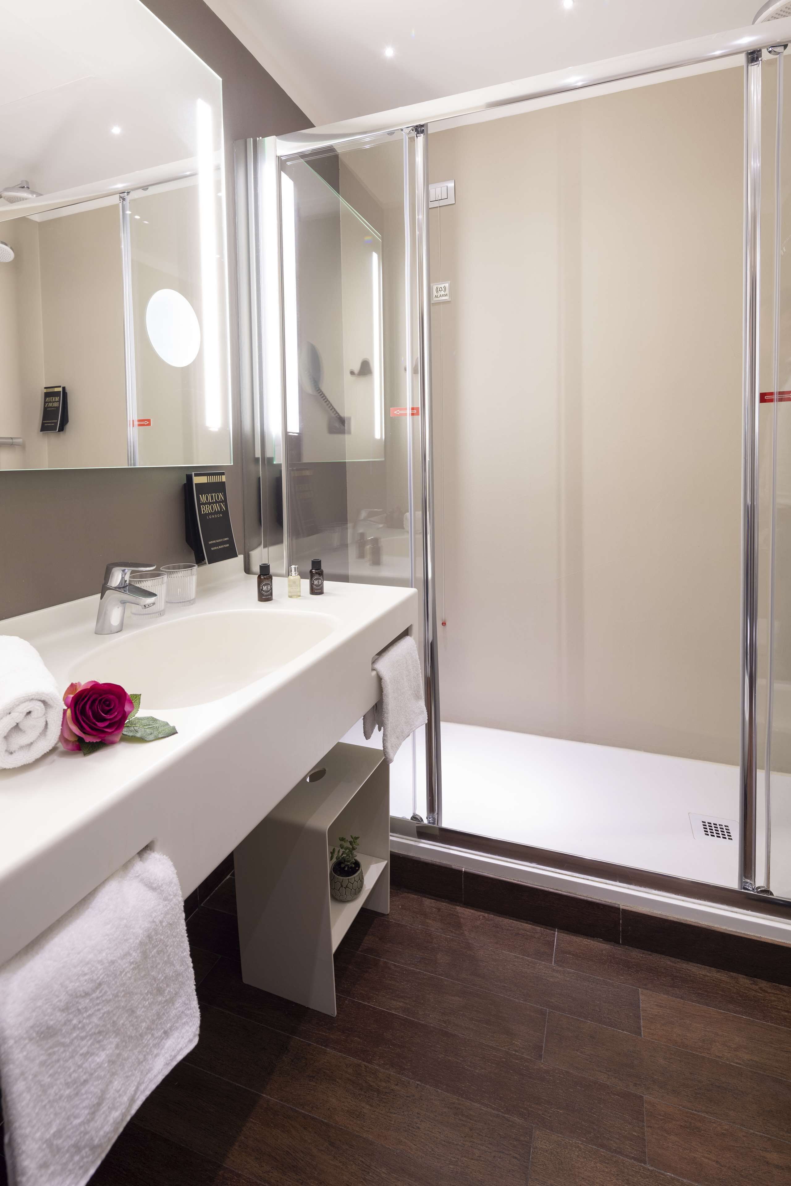 Un baño moderno con lavamanos blanco, cabina de ducha de vidrio y un espejo grande.