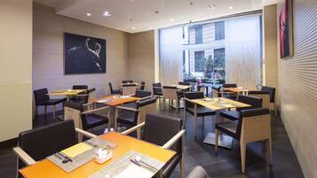 A modern dining area with multiple tables and chairs, a large window with a view of the outside, and a wall-mounted artwork.
