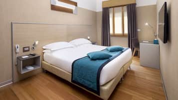 A hotel room with a bed, bedside table, lamp, and a TV on the wall.
