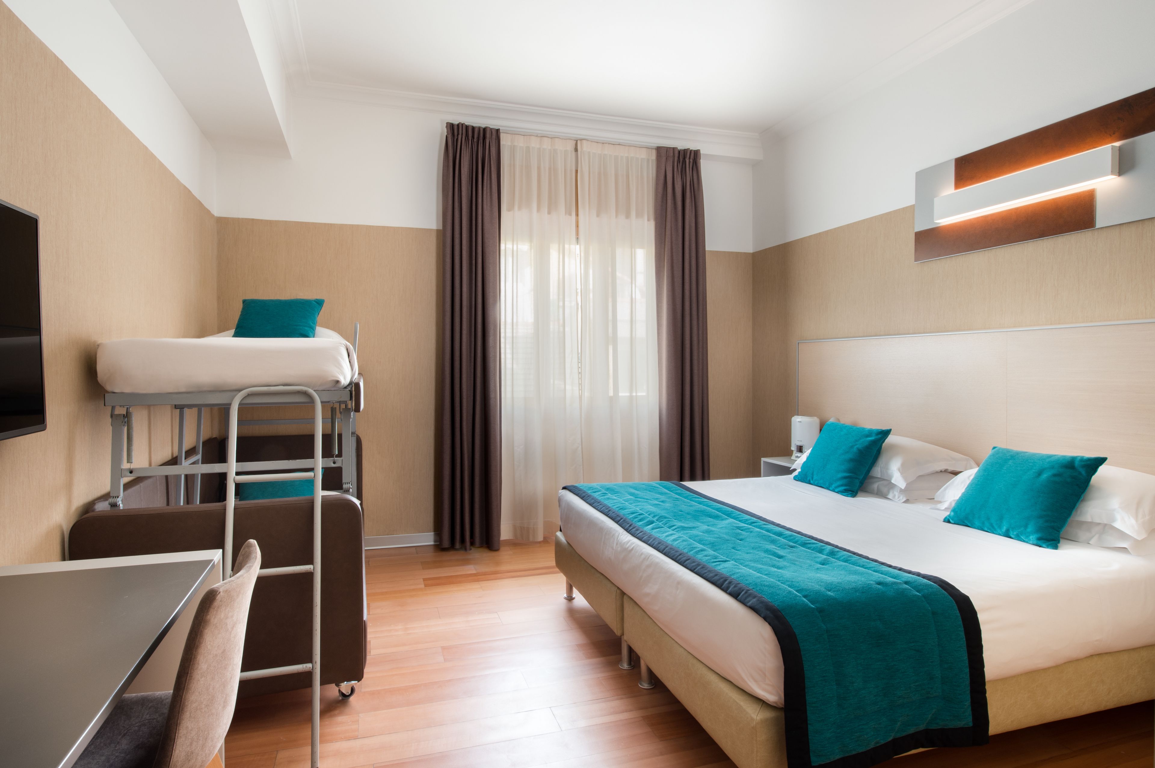 Quarto de hotel com beliche, uma escrivaninha e uma cadeira.