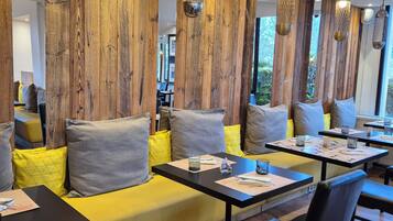 Ein modernes Restaurant mit Holzwandverkleidung, gelb gepolsterten Sitzgelegenheiten, schwarzen Tischen und hängenden Pendelleuchten.