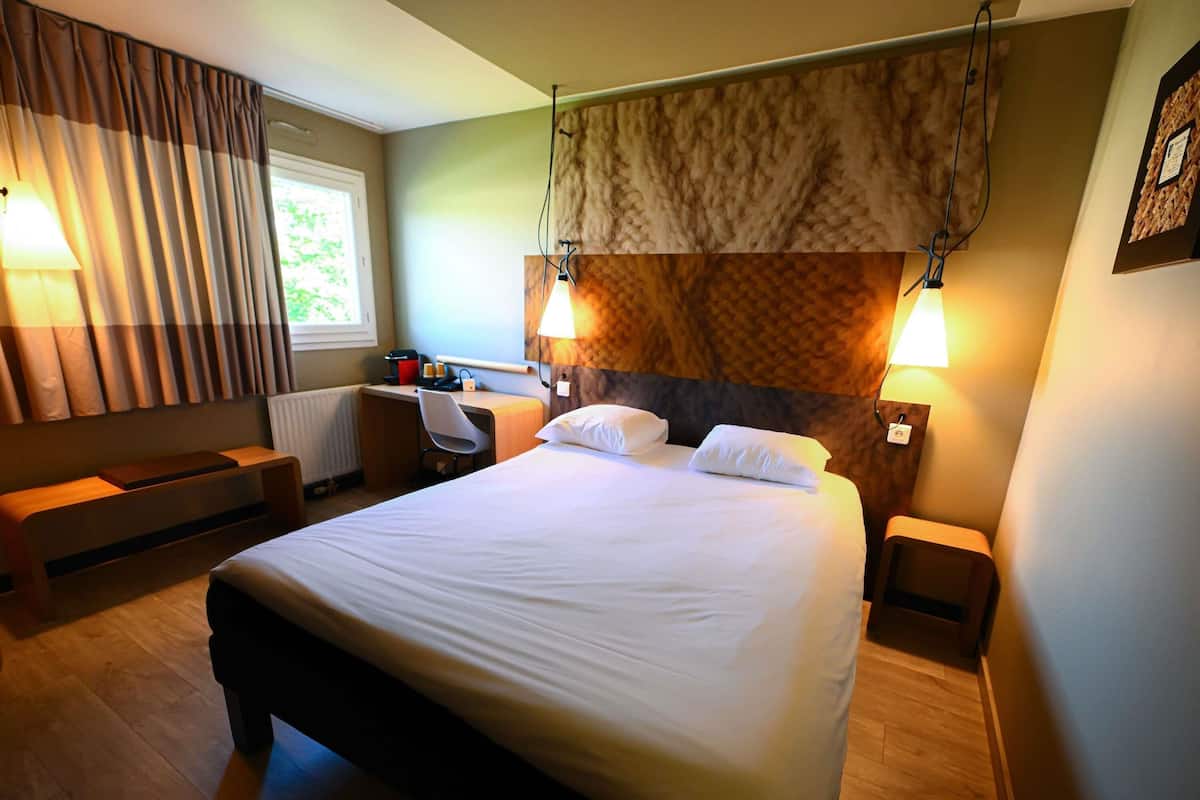 A hotel room with a large bed, a desk, a chair, and two bedside lamps.