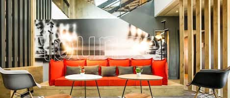 A modern lounge area with a red sofa, two round tables, and black chairs.