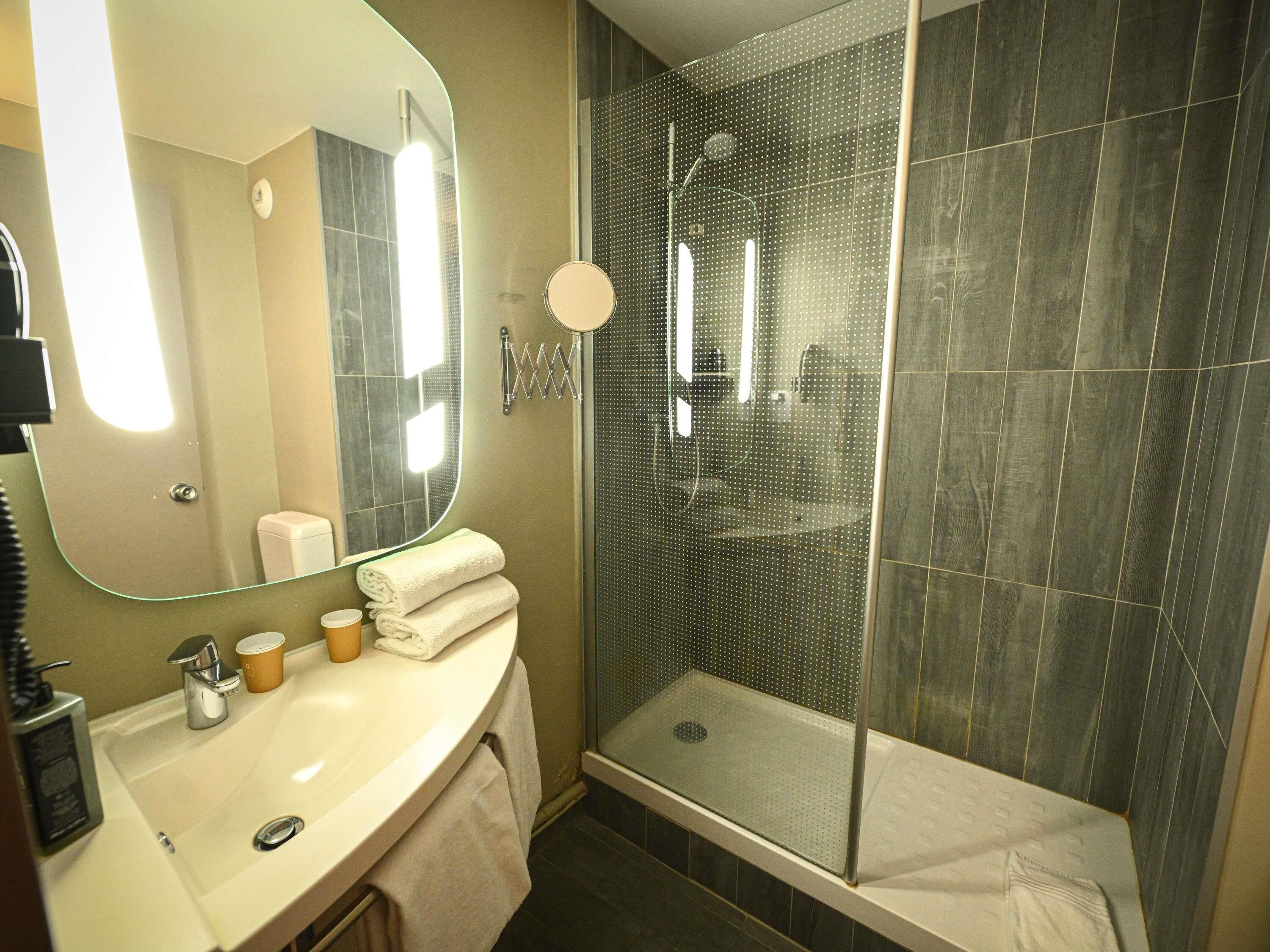 Ein Badezimmer mit Waschbecken, Spiegel, Handtuchhalter und Duschkabine.