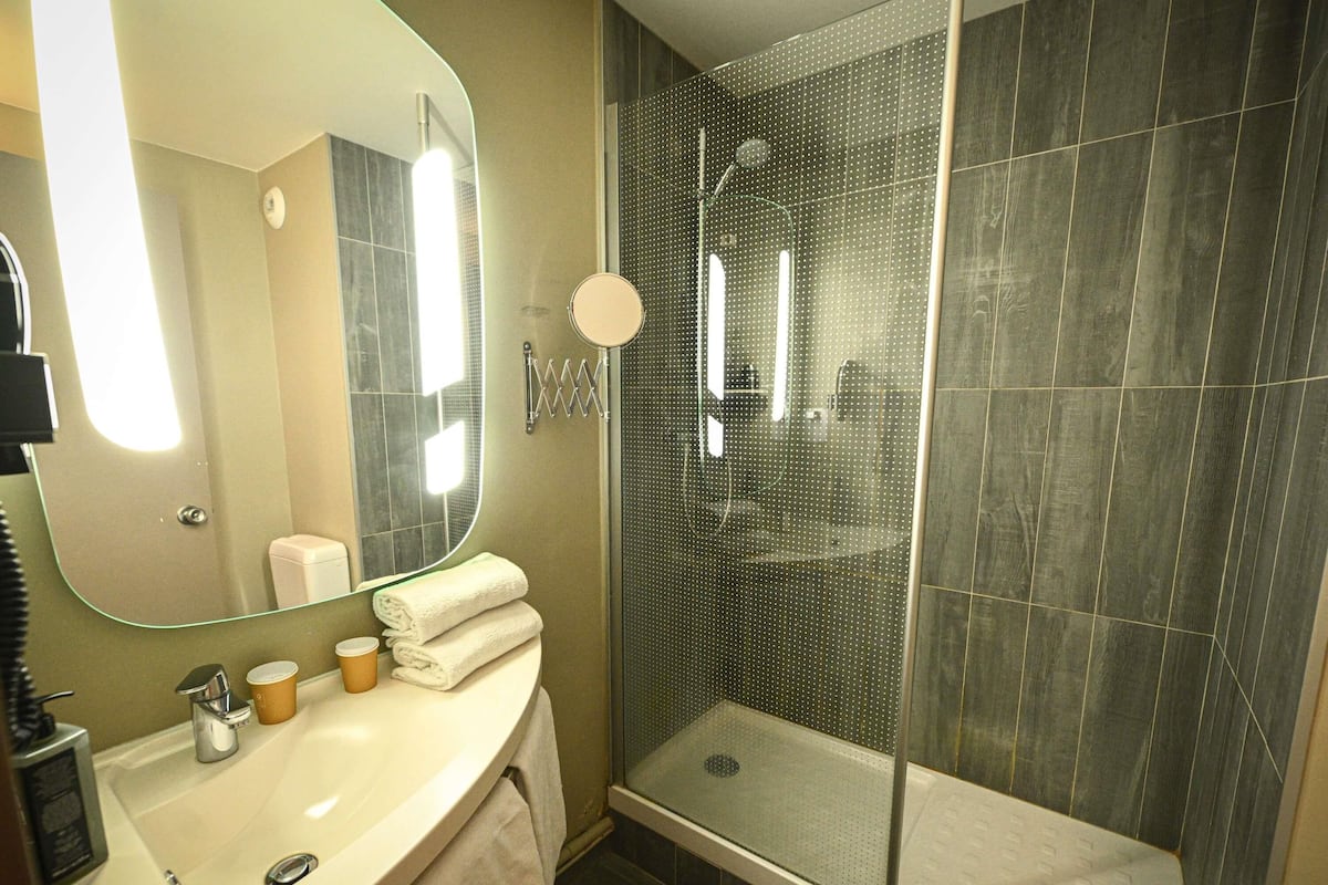 Ein Badezimmer mit Waschbecken, Spiegel, Handtuchhalter und Duschkabine.