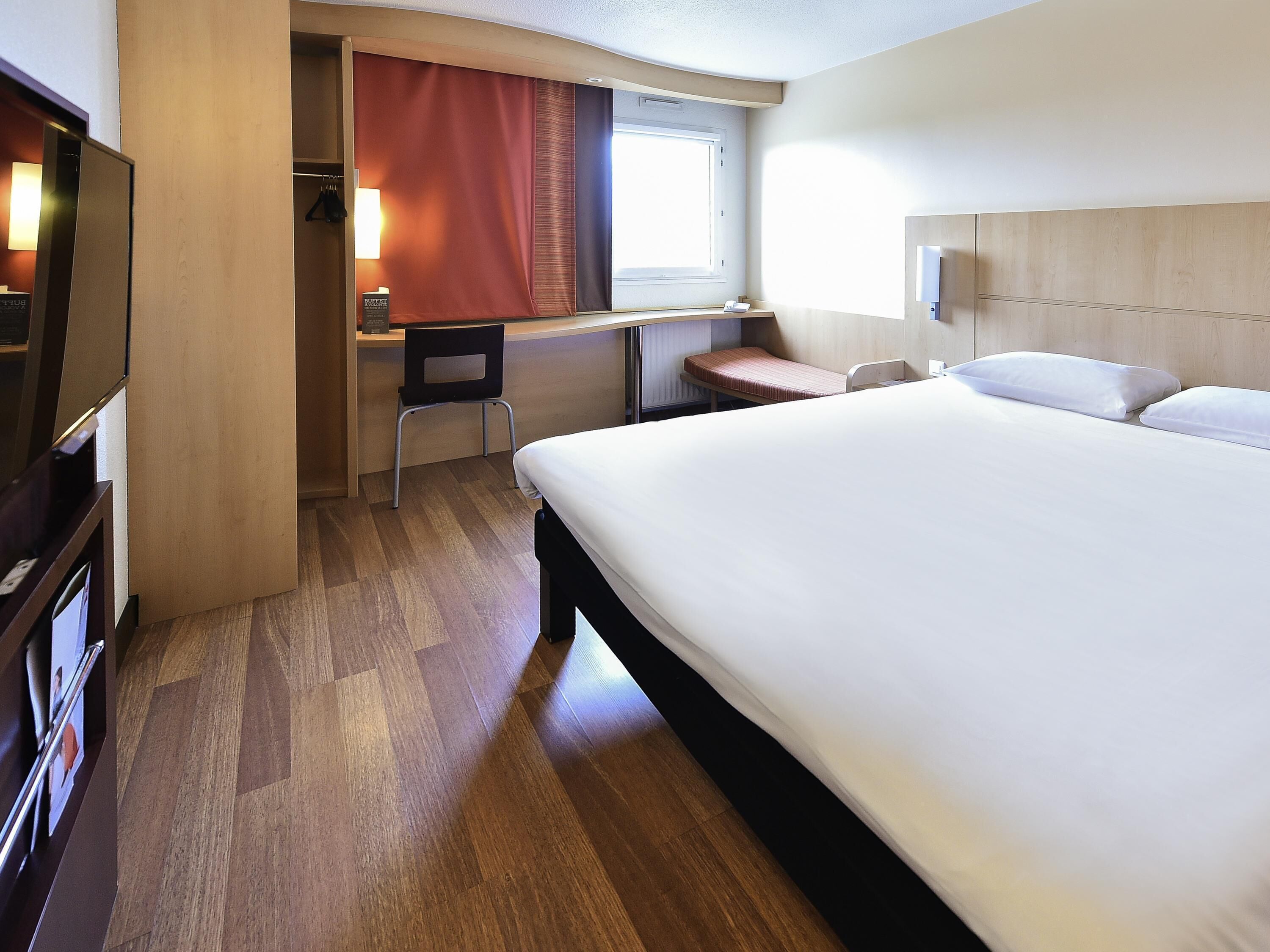 A hotel room with a bed, a desk, a chair, and a television.