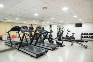 Un gimnasio con cintas de correr, bicicletas estáticas y un banco para pesas.