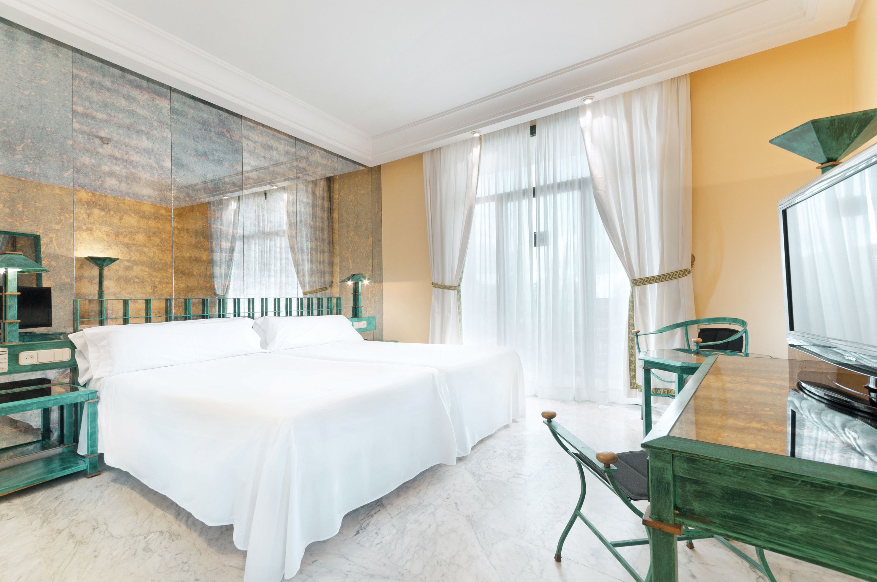 A hotel room with a large bed, a glass table, a chair, a TV, and a mirror.