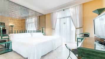 A hotel room with a large bed, a glass table, a chair, a TV, and a mirror.