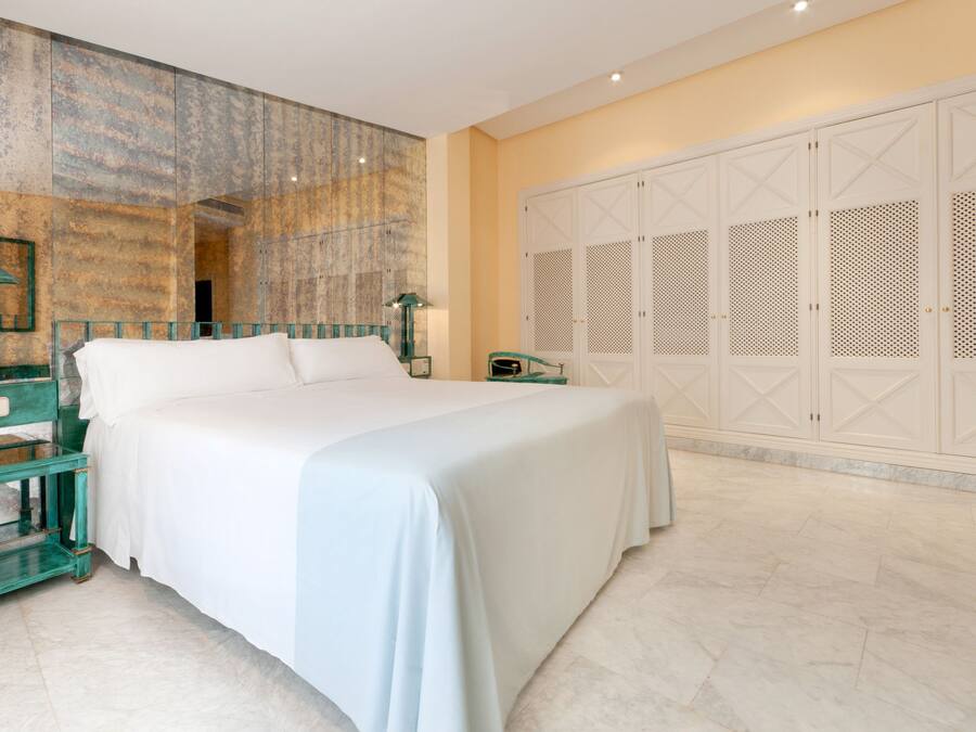 Un dormitorio amplio con una cama grande, una mesita de noche, una lámpara y un armario con puertas batientes.