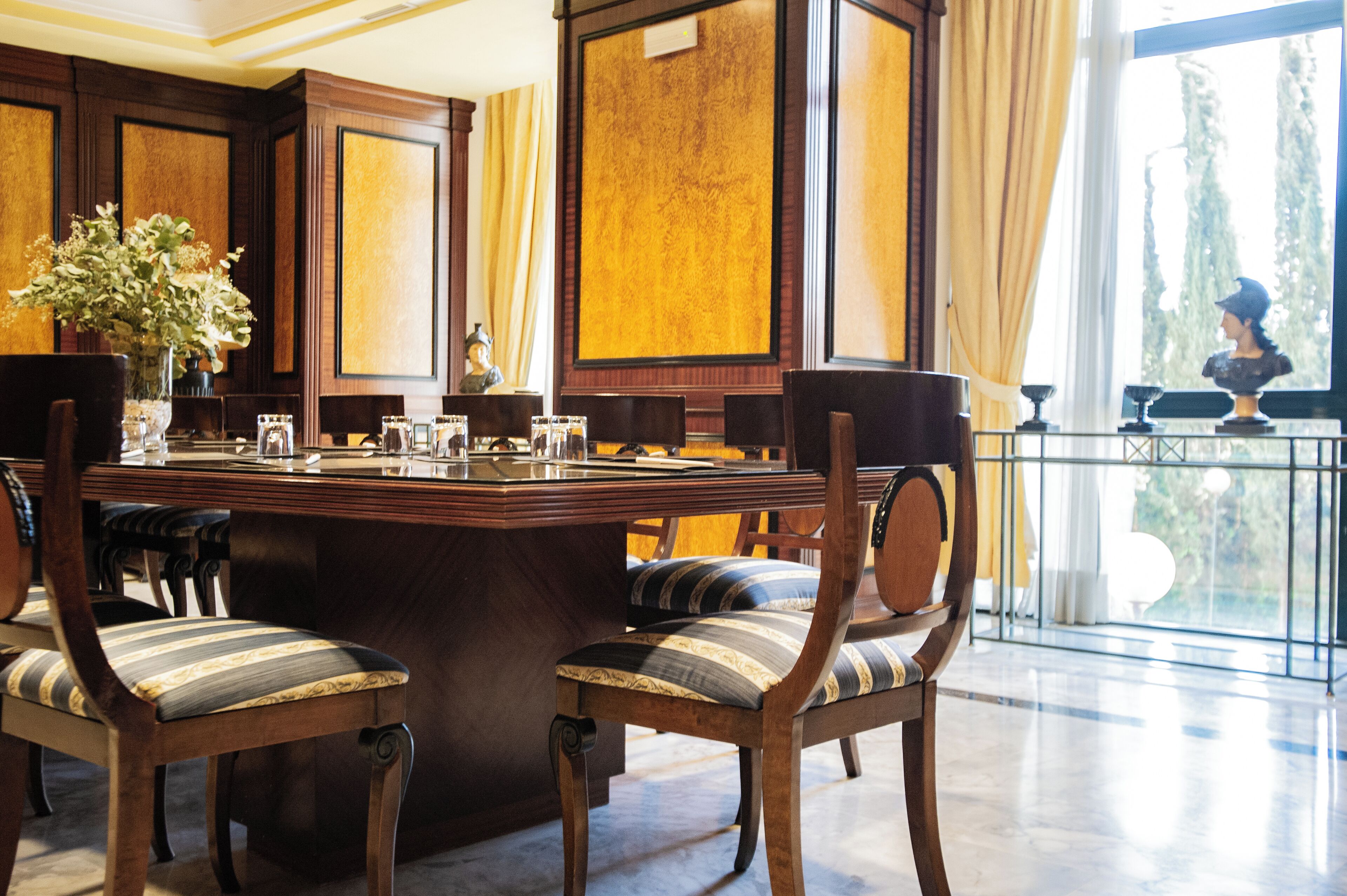 A formal dining area with a large wooden table, striped upholstered chairs, and a vase of flowers.