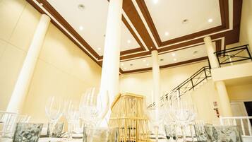 Un salón de banquetes con techo alto, vigas de madera y una escalera al fondo.