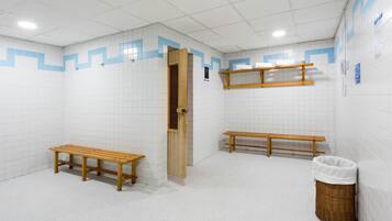 En offentlig toilet med hvide fliservægge, træbænke, en skraldespand og en hylde med håndklæder.