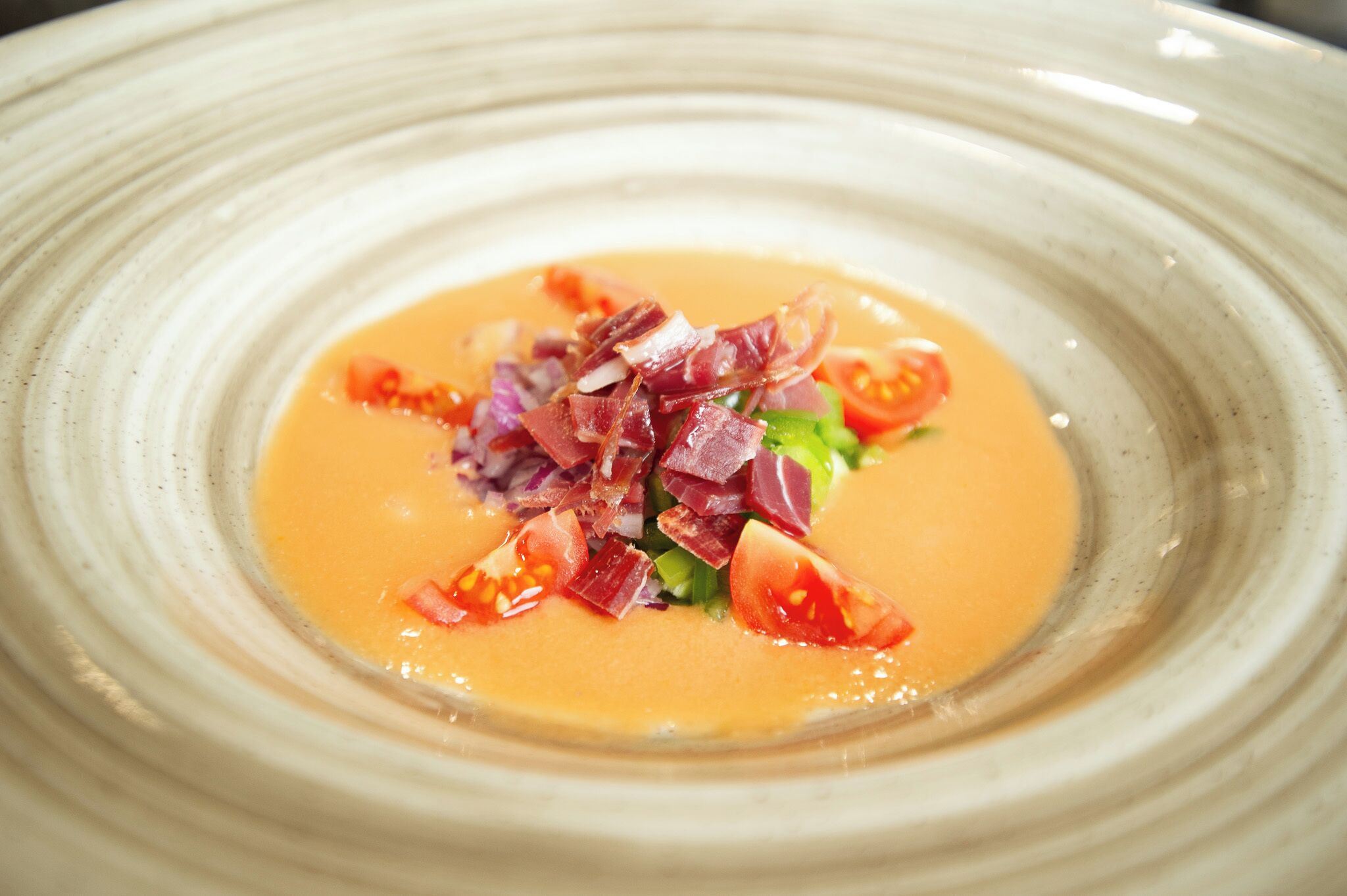 Un plato con sopa cremosa color naranja, adornado con cebollas rojas, tomates cherry y hierbas verdes.