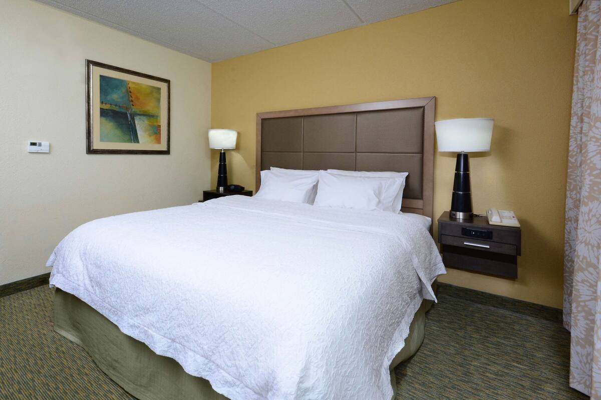 A hotel room with a large bed, two bedside lamps, a nightstand, a painting on the wall, and a telephone on the nightstand.