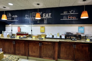 A kitchen area with a chalkboard wall displaying food-related drawings and text, a counter with various food items and a sign labeled "EGGS", and wooden cabinets below.
