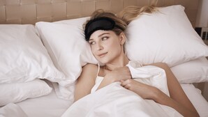 En person ligger i sängen, omgiven av vita sängkläder och kuddar.