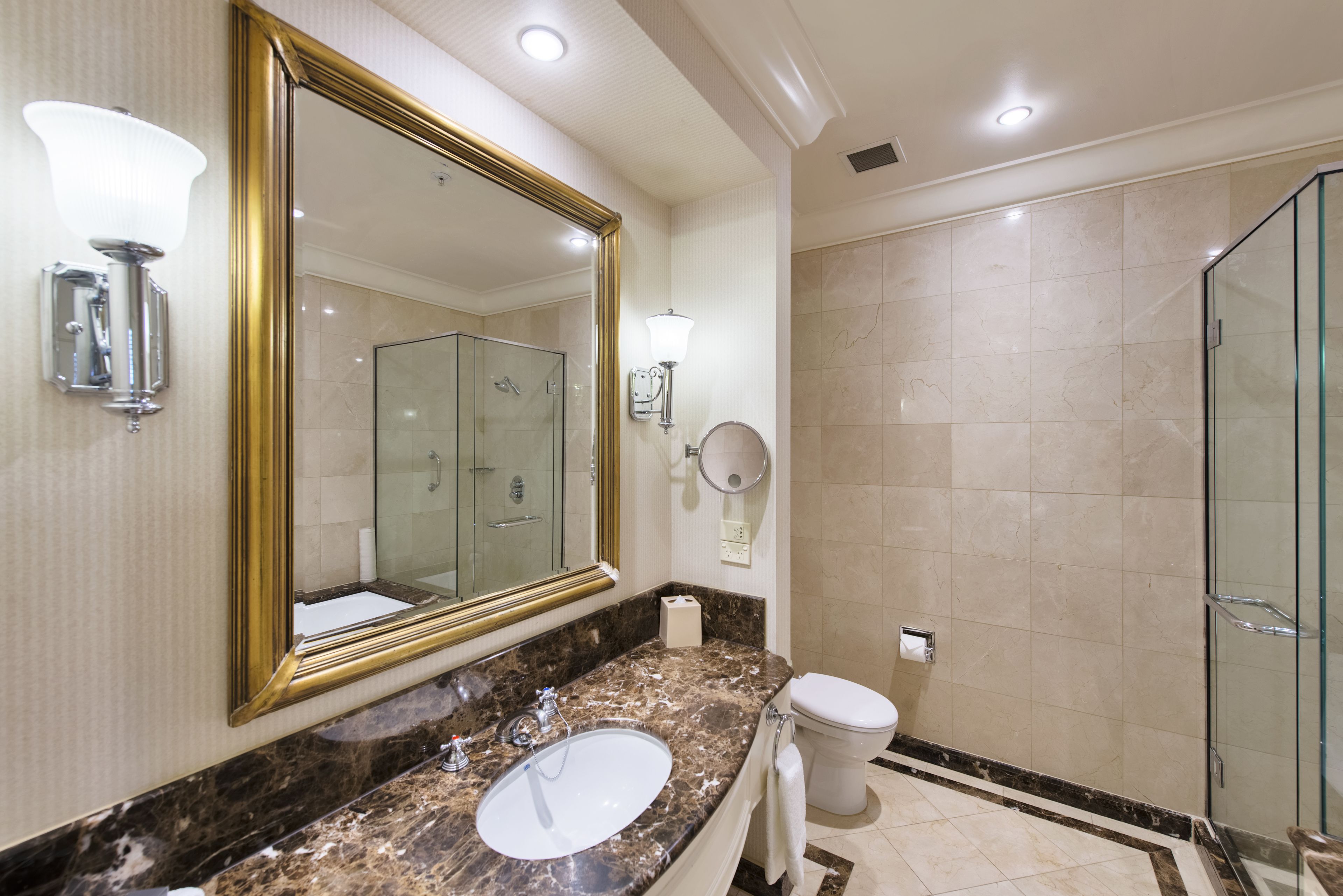 A modern bathroom with a large mirror, a marble sink, a toilet, and a glass-enclosed shower.