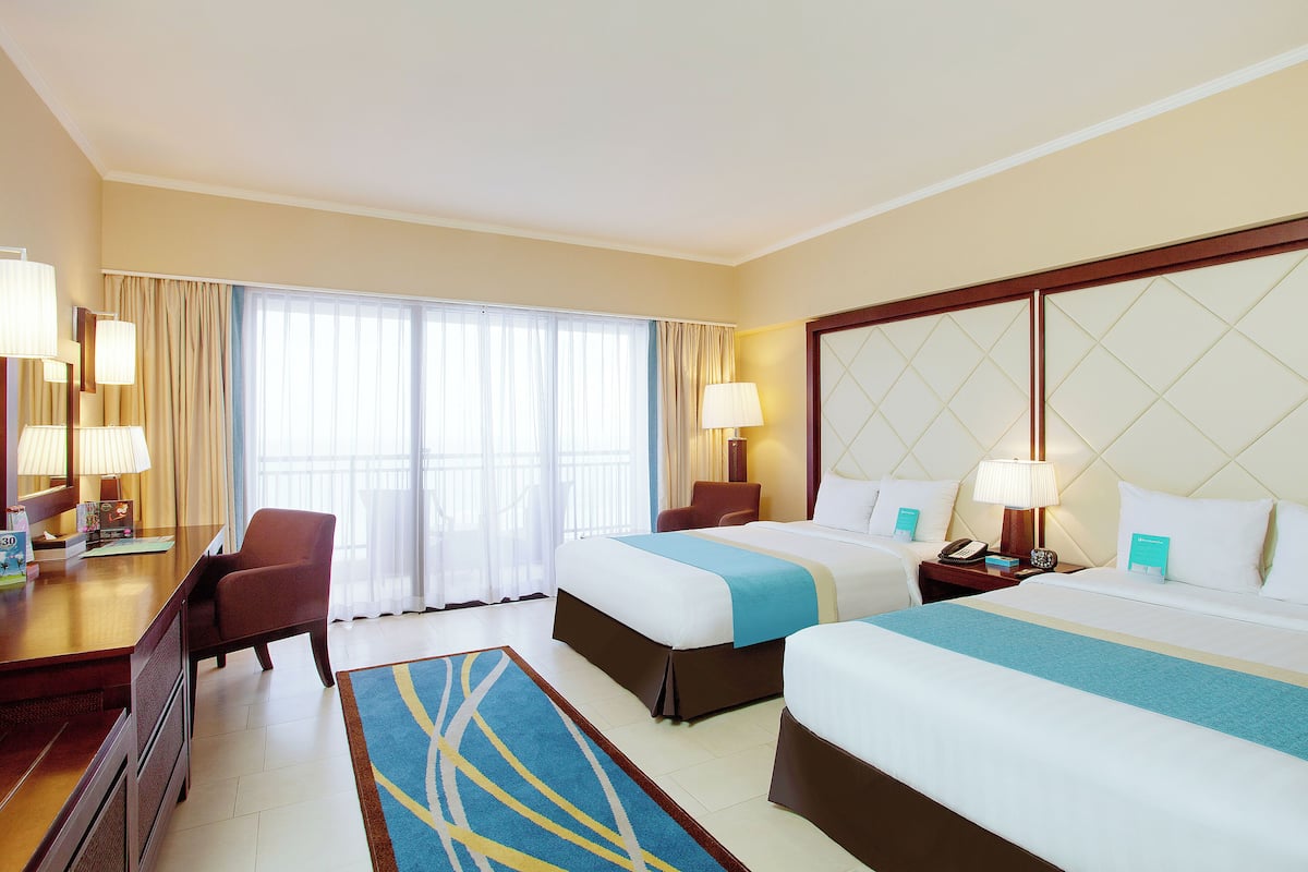 A hotel room with two beds, a desk, a chair, and a large window with curtains.