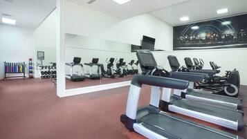 Un gimnasio con cintas de correr, máquinas de pesas y un muro de espejos.