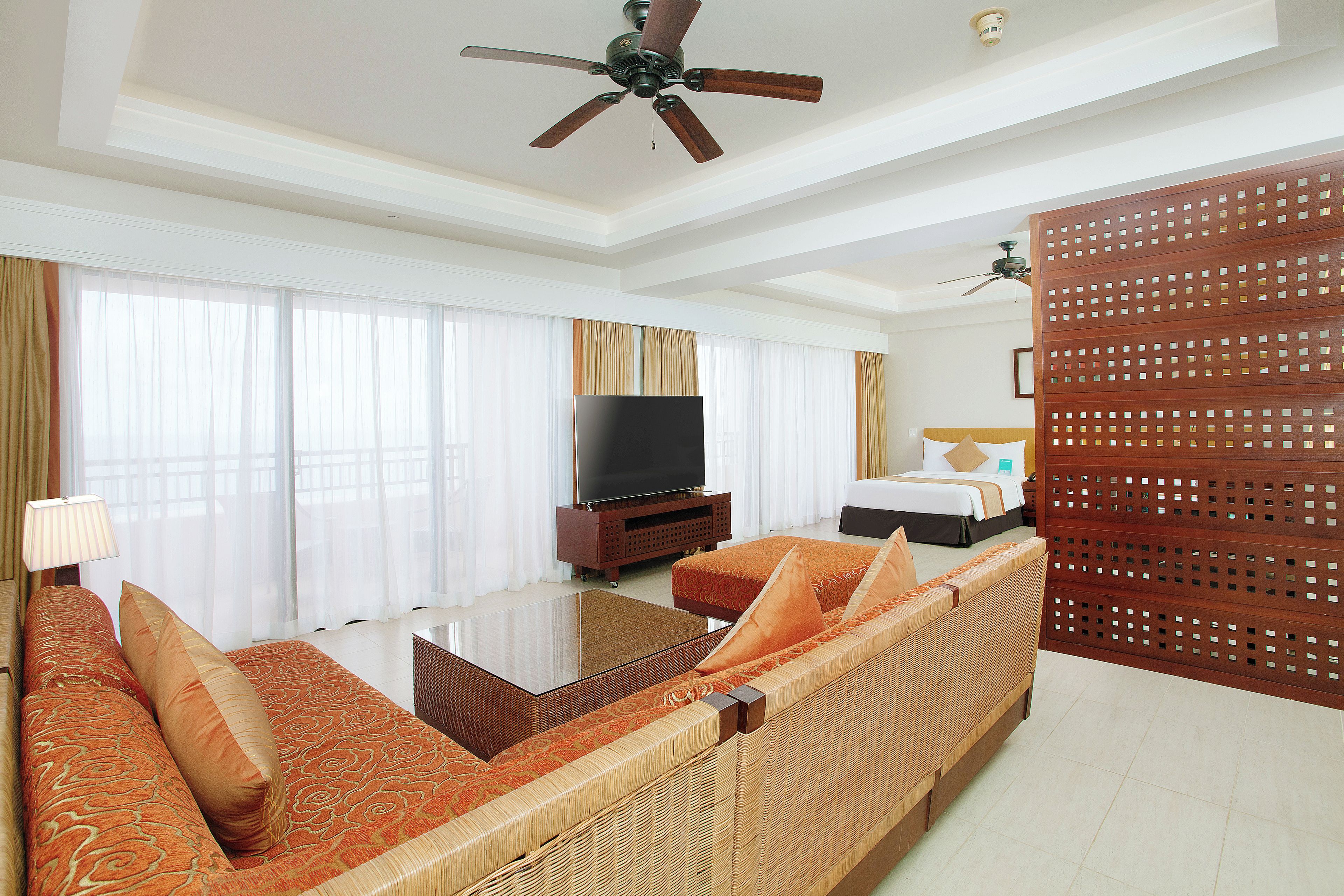 A hotel room with a large bed, a television, a sofa, and a ceiling fan.