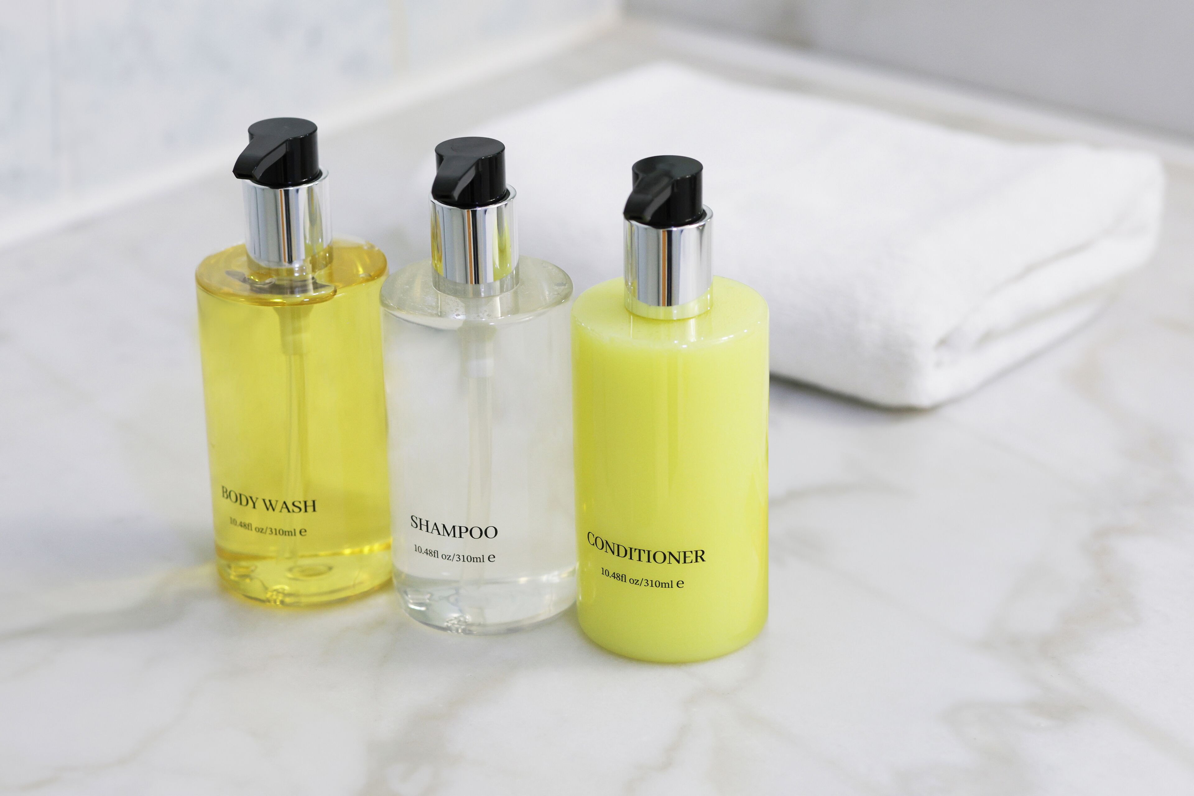 Three bottles of body wash, shampoo, and conditioner on a marble surface.