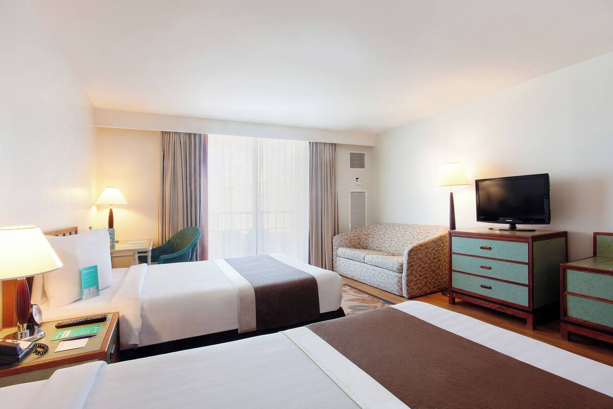 A hotel room with two beds, a television, a desk with a lamp, a chair, and a dresser.