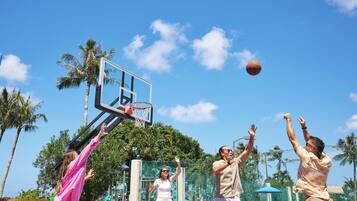 Una cancha de baloncesto con aro, palmeras y cielo despejado.