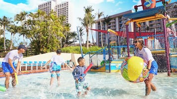 A water park with a play structure, palm trees, and a building in the background.