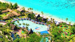 An aerial view of a resort with a large swimming pool, beach, and tropical landscaping.