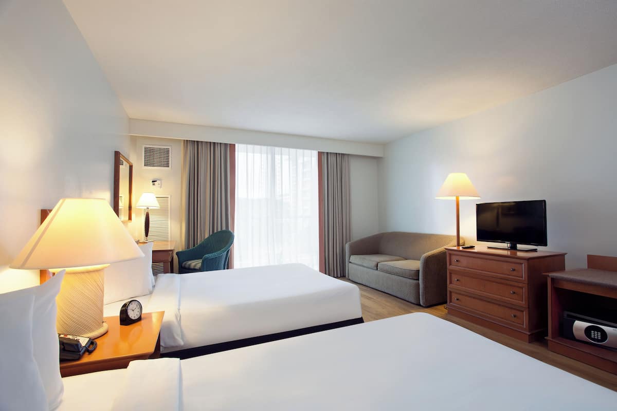 A hotel room with two beds, a TV, a desk with a lamp, a chair, and a sofa.