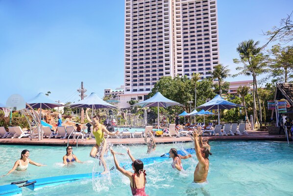 A pool area with lounge chairs, umbrellas, and a tall building in the background.