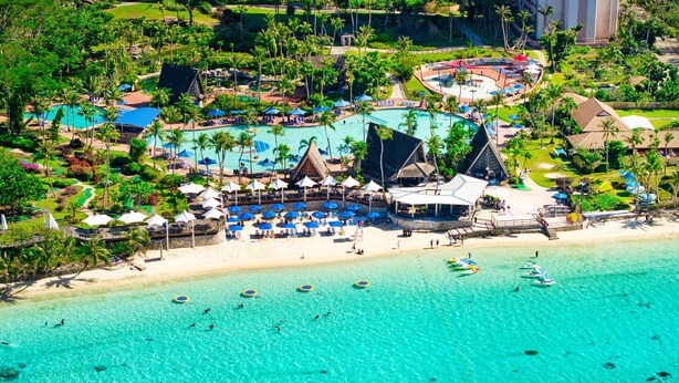 A resort with a large pool, beach area, and multiple umbrellas.