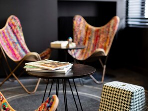 Una habitación moderna con dos sillas coloridas, una mesita redonda y un otoman estampado.