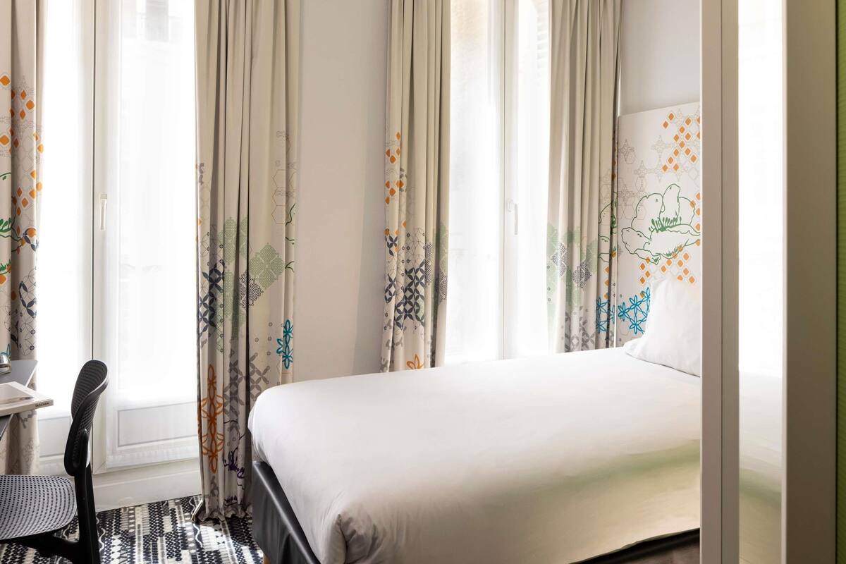 Une chambre d’hôtel avec un lit, un bureau et des rideaux à motifs géométriques.