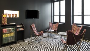 Ein modernes Zimmer mit einem schwarz-weißen Fußboden, einem an der Wand montierten Flachbildfernseher und zwei bunten Stühlen um einen kleinen Tisch.