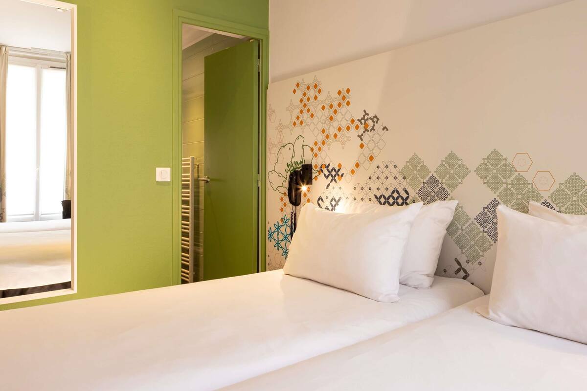 Une chambre d’hôtel avec un lit, une porte verte et un mur orné de motifs géométriques.