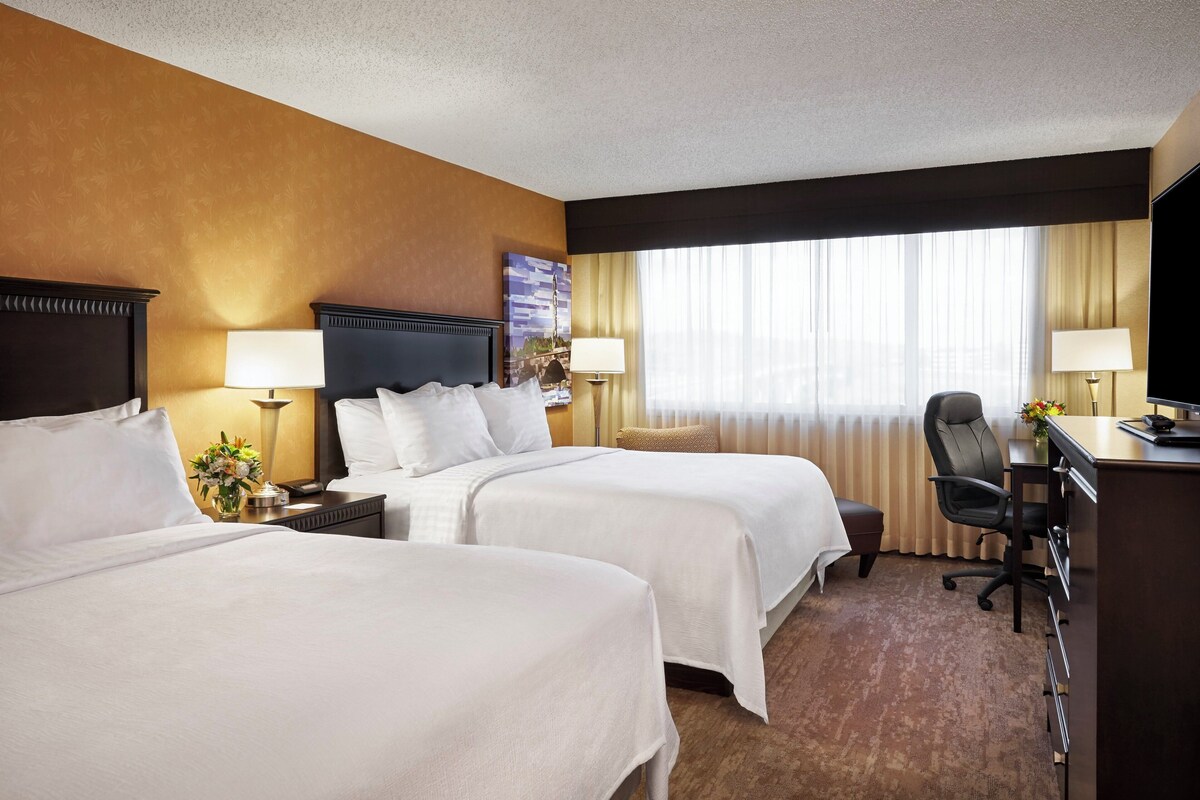 A hotel room with two beds, a desk, a chair, and a television.