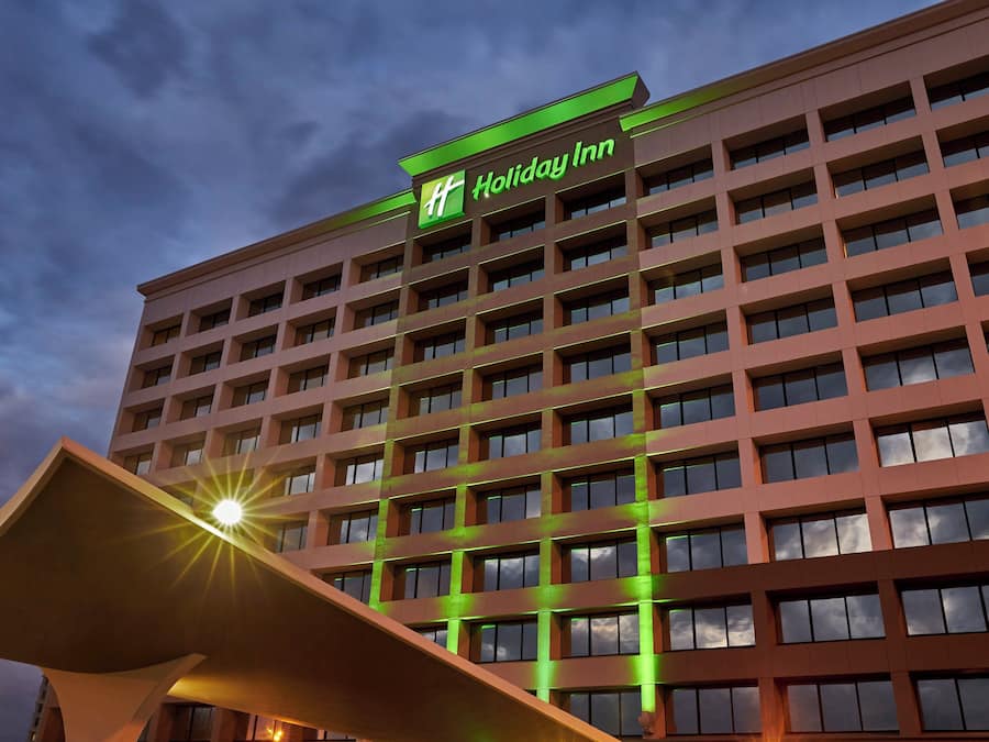Edificio de un hotel Holiday Inn con un llamativo letrero verde, varios pisos y un diseño arquitectónico moderno.