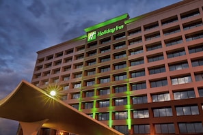 A Holiday Inn hotel building with a prominent green sign, multiple floors, and a modern architectural design. - Holiday Inn Alexandria at Carlyle by IHG (Alexandria)