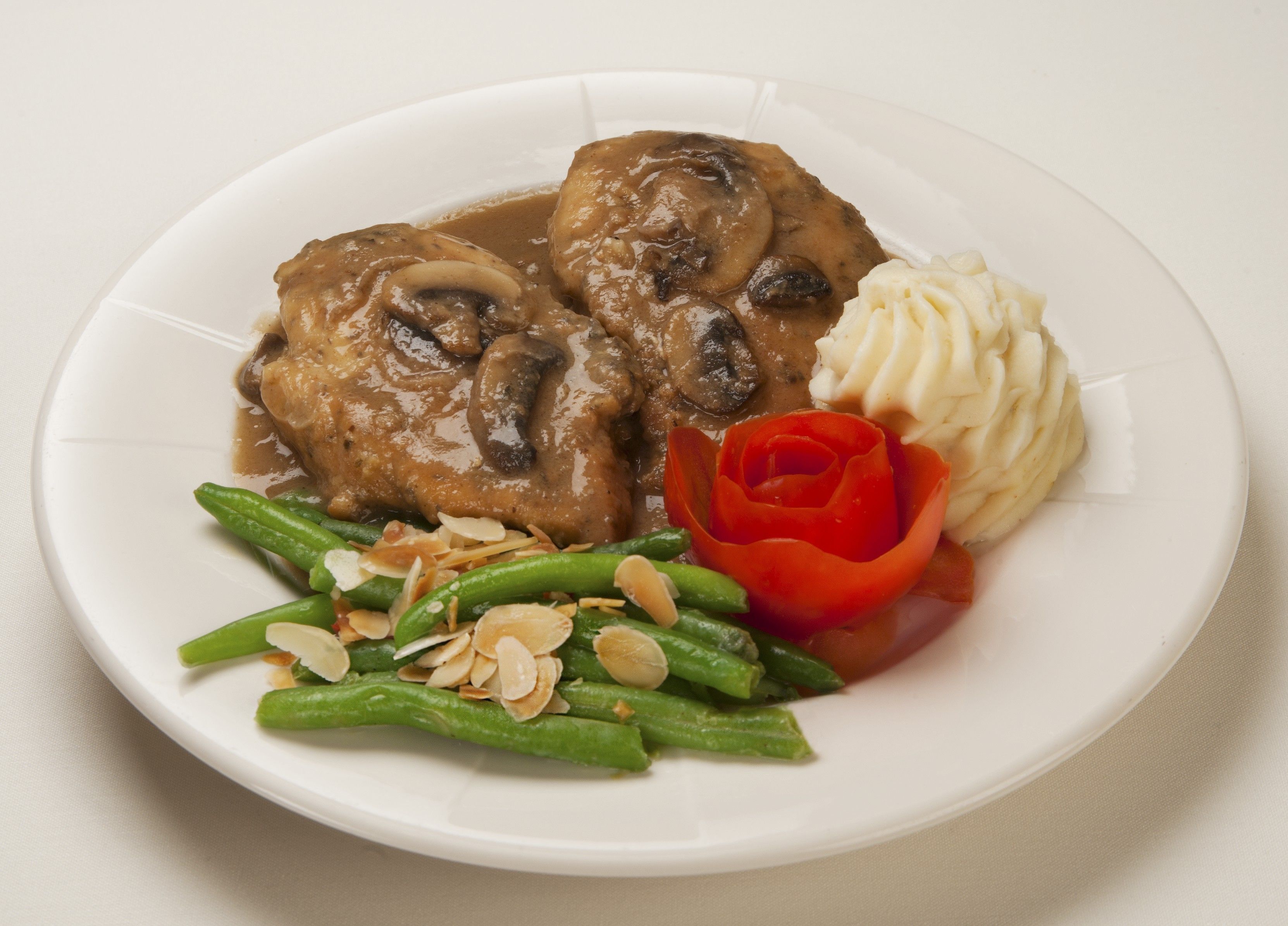 A plate with a meat dish, mashed potatoes, green beans, and a decorative red flower.