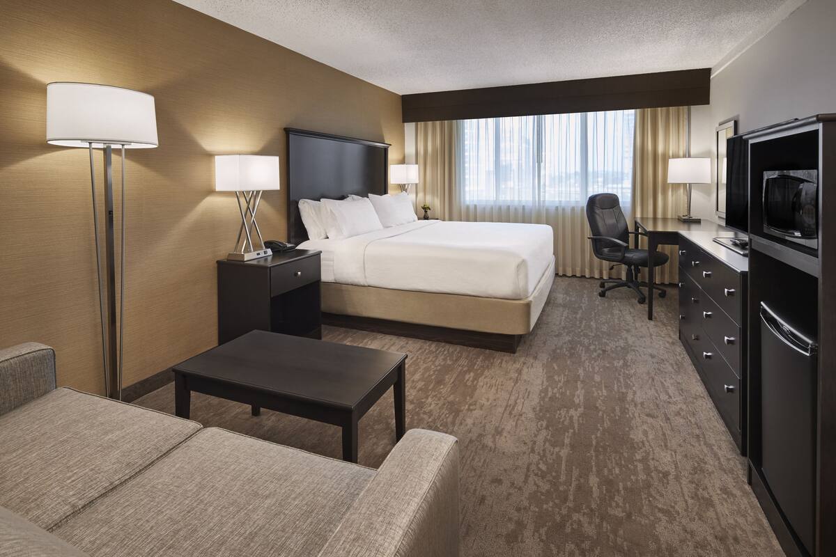 A hotel room with a bed, a desk, a chair, a TV, and a lamp.