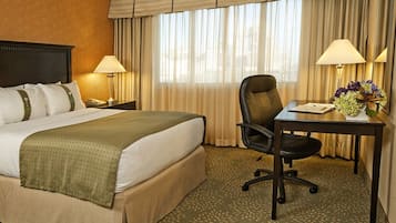 Una habitación de hotel con una cama grande, un escritorio con una silla, dos lámparas y un jarrón con flores.