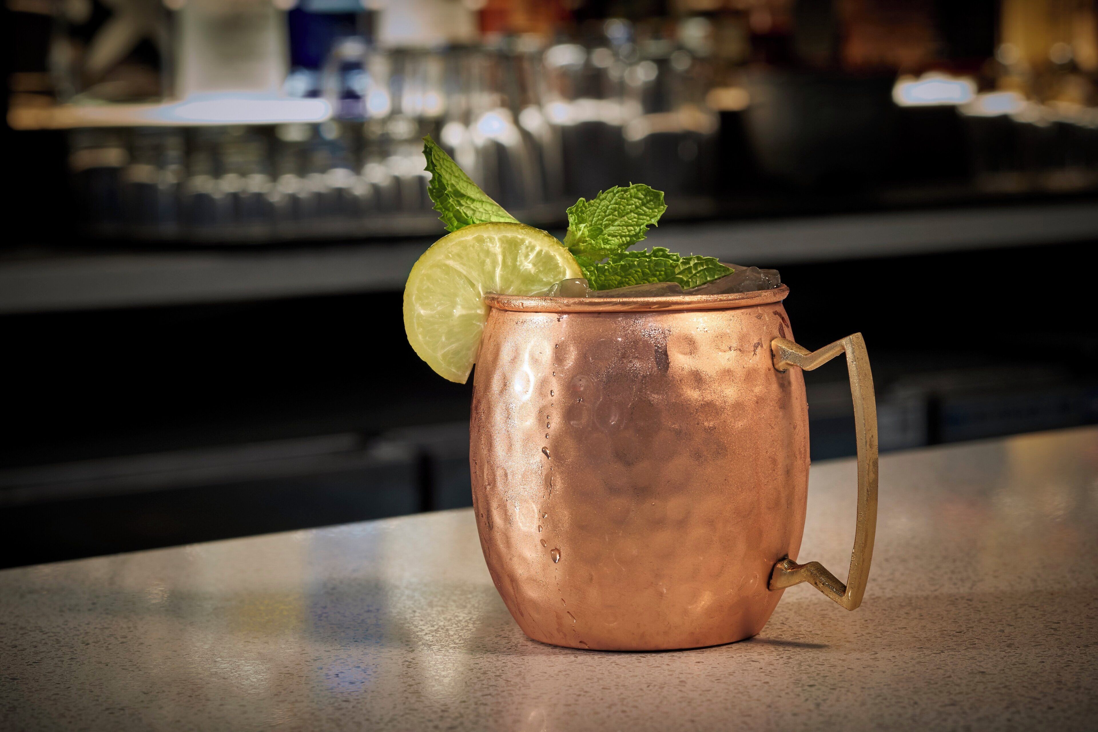 A copper mug with a handle, containing a beverage garnished with a lime slice and mint leaves, placed on a bar counter.