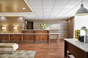 A hotel reception area with a wooden reception desk, a sofa, a patterned rug, and a large window with a view. - Holiday Inn Alexandria at Carlyle by IHG (Alexandria)
