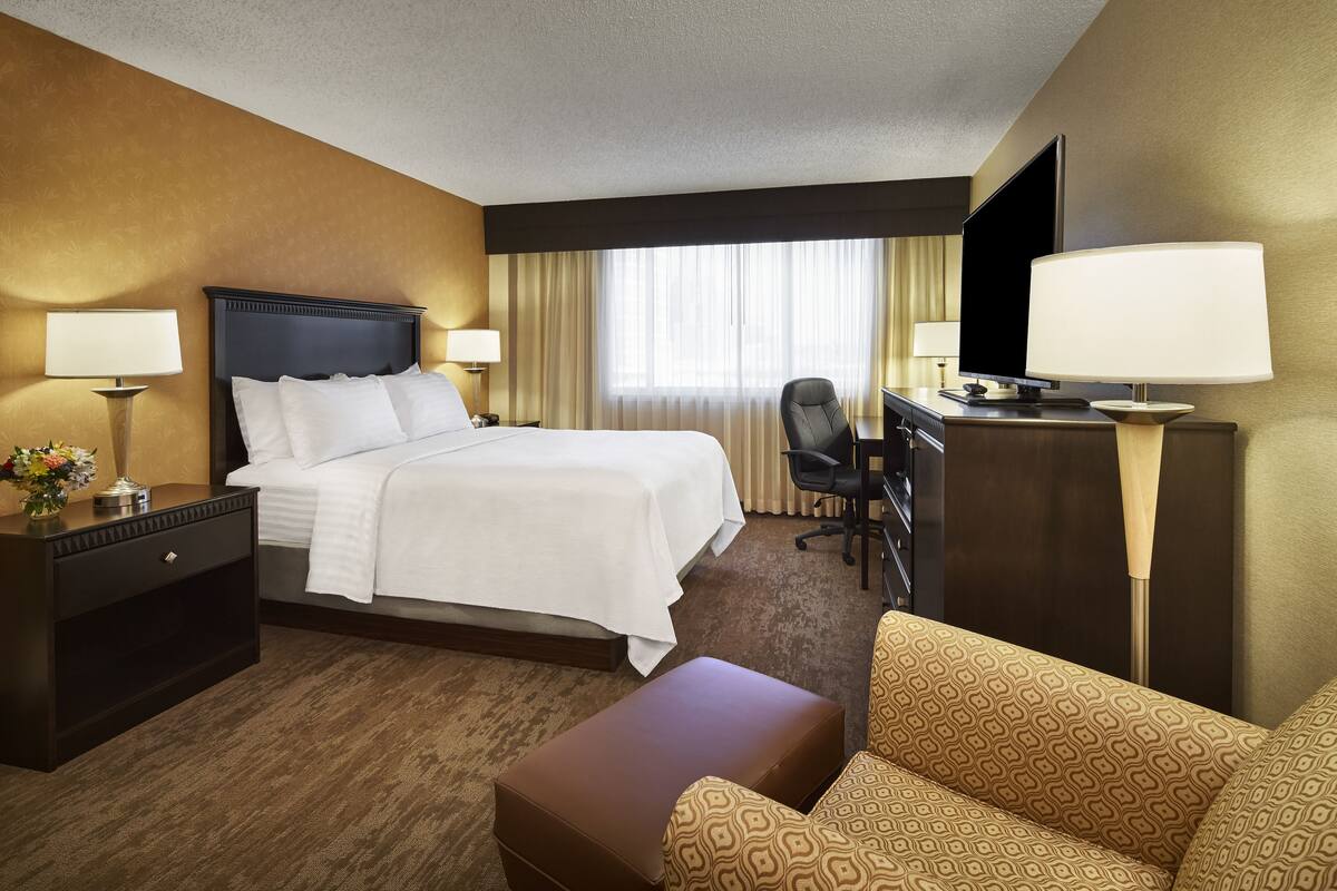 A hotel room with a bed, a desk, a chair, a TV, and a sofa.