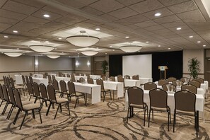 A conference room with multiple tables and chairs, arranged in rows, with a carpeted floor and ceiling lights. - Holiday Inn Alexandria at Carlyle by IHG (Alexandria)