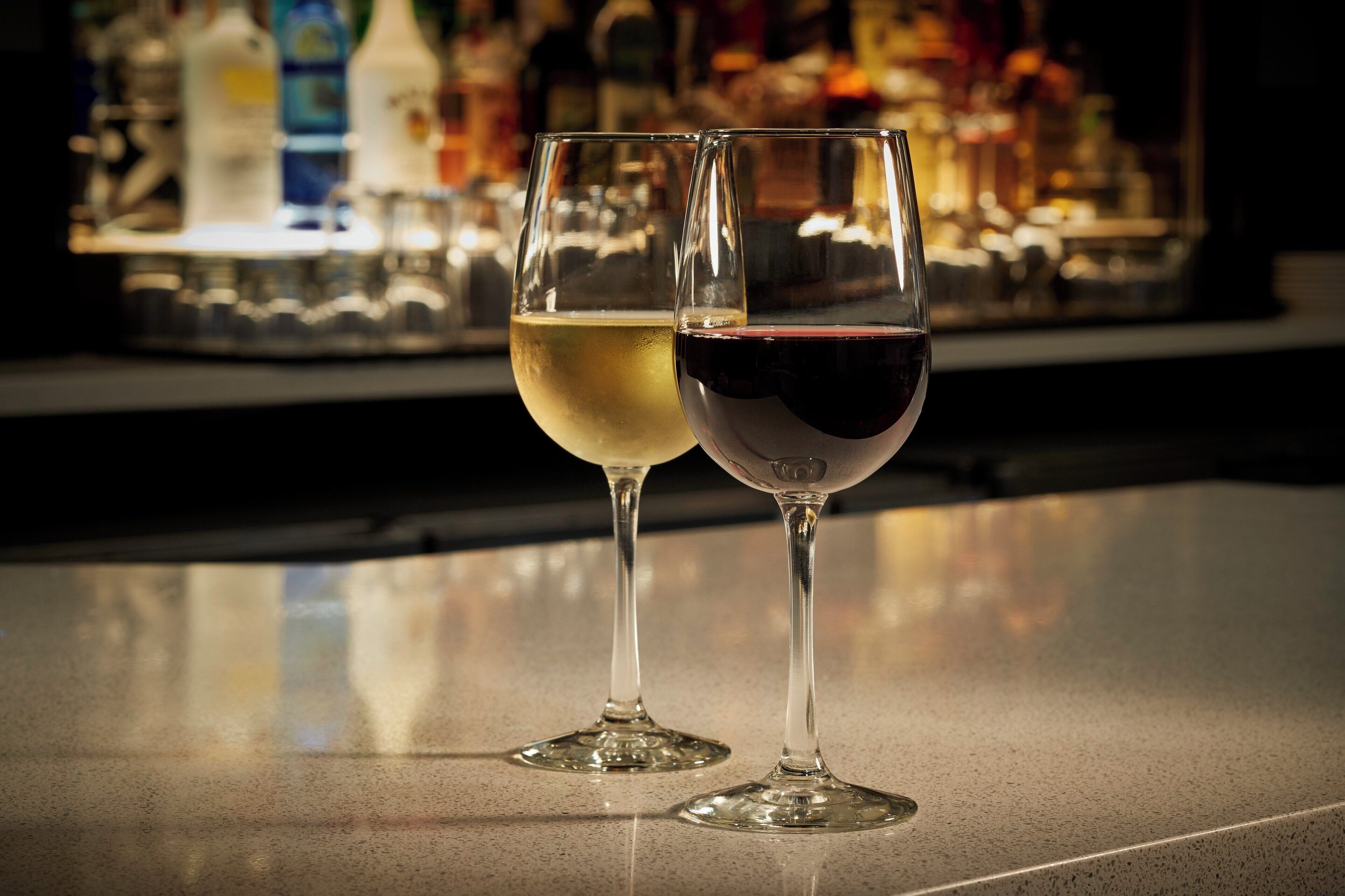 Dos copas de vino sobre una barra con un fondo desenfocado de botellas.