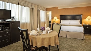 Une chambre d’hôtel comprenant un lit, une table de chevet, une lampe, une télévision et un coin repas avec une table dressée pour deux personnes.