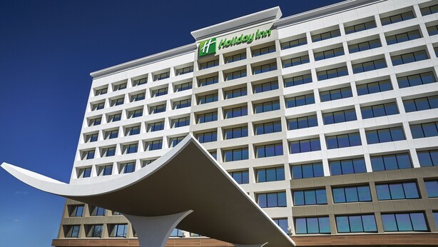 A Holiday Inn hotel building with a modern design, featuring a prominent logo on the facade. - Holiday Inn Alexandria at Carlyle by IHG (Alexandria)